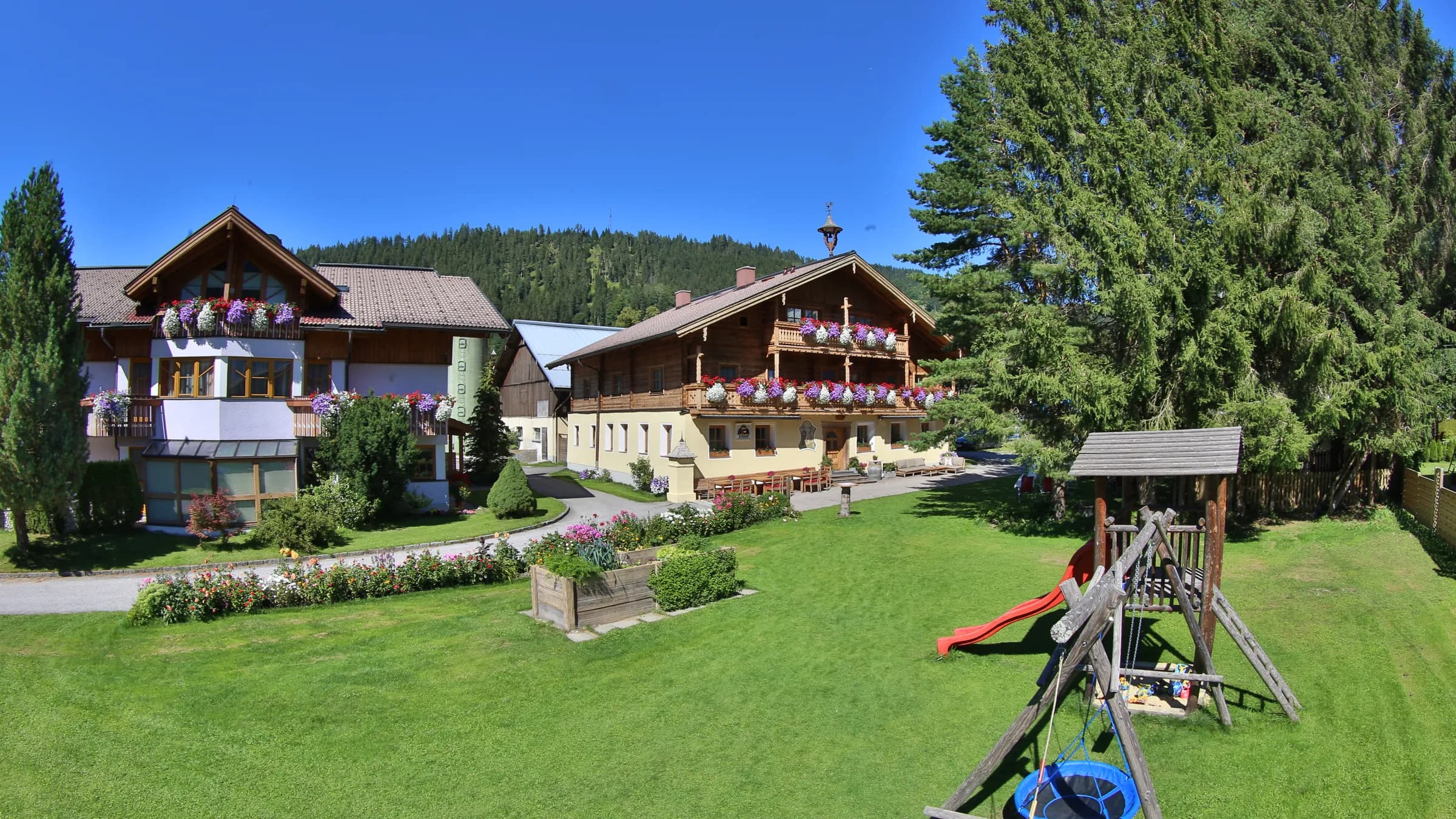 Blick über die Spielwiese mit Spielturm auf Landhaus und Bauernhaus des Ferienhofs Kasparbauer in Radstadt